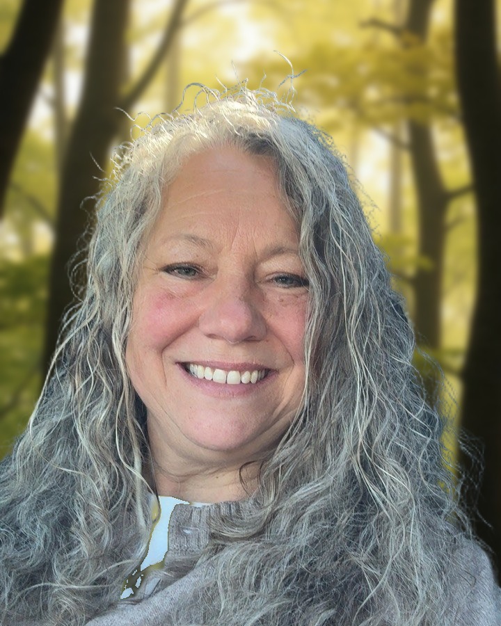 Myli Taylor smiling, with long curly silver hair, in front of sunlit woods